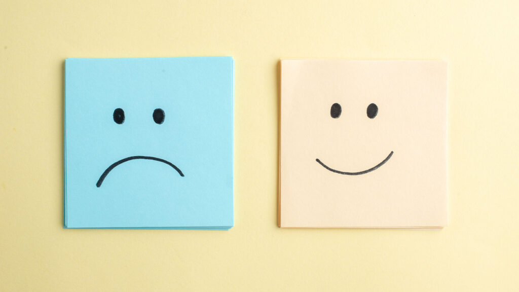 Ein Bild mit zwei Post-It-Stapeln. Der linke, blaue Stapel hat einen traurigen aufgemalten Smiley. Der rechte, gelbe Stapel hat einen fröhlichen aufgemalten Smiles. Es symbolisiert die zwei Seiten eines inneren Konfliktes, den man mit TCM lösen kann.